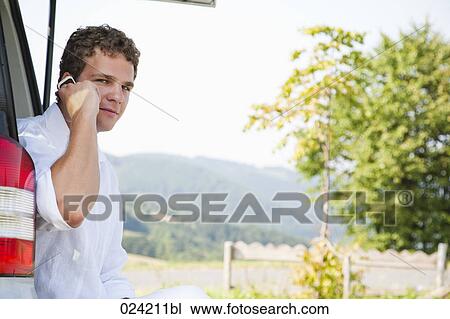 Stock Image - portrait of young man in trunk of car with mobile phone. Fotosearch