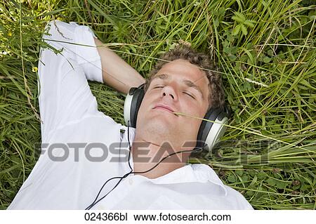 Stock Image - portrait of young man lying in grass listening to music. Fotosearch