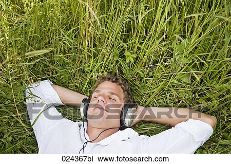 Stock Image - portrait of young man lying in grass listening to music. Fotosearch