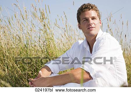 Stock Image - portrait of young man sitting in meadow. Fotosearch