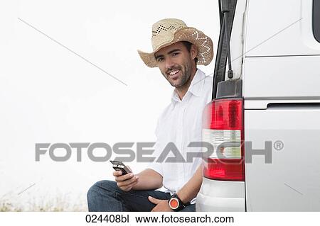 Stock Image - portrait of young man wearing straw hat with mobile phone. Fotosearch