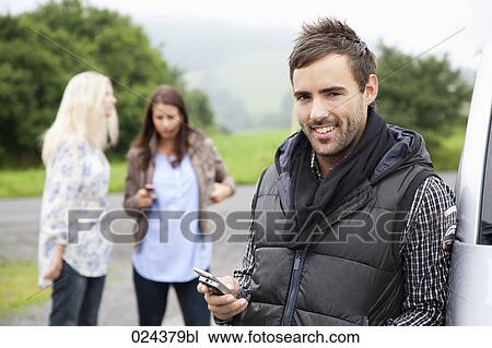 Stock Image - portrait of young man with mobile phone at car. Fotosearch