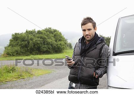 Stock Image - portrait of young man with mobile phone at car. Fotosearch