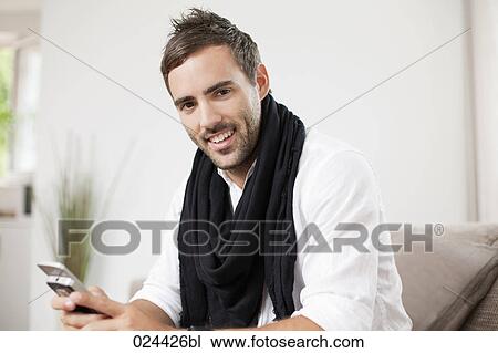 Stock Image - portrait of young man with mobile phone sitting at home. Fotosearch