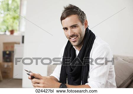 Stock Image - portrait of young man with mobile phone sitting at home. Fotosearch