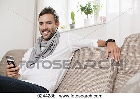 Stock Image - portrait of young man with mobile phone sitting at home. Fotosearch