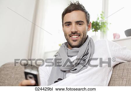 portrait of young man with mobile phone sitting at home View Large Photo Image Stock Image - portrait of young man with mobile phone sitting at home. Fotosearch