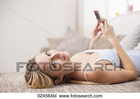 portrait of young woman at home lying on sofa with mobile phone View Large Photo Image Stock Image - portrait of young woman at home lying on sofa with mobile phone. Fotosearch