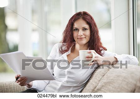 Stock Image - portrait of young woman at home with documents and coffee cup. Fotosearch