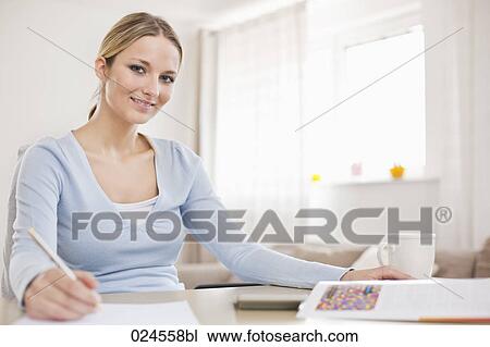 Stock Image - portrait of young woman at home working at table. Fotosearch