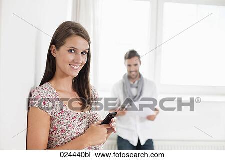Stock Image - portrait of young woman in empty room with mobile phone. Fotosearch