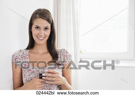 Stock Image - portrait of young woman in empty room with mobile phone. Fotosearch
