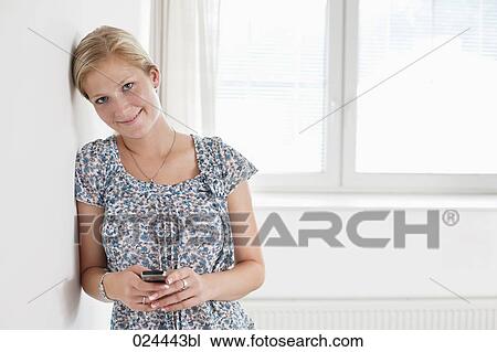 Stock Image - portrait of young woman in empty room with mobile phone. Fotosearch