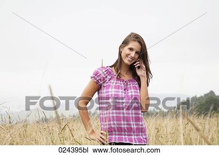 Stock Image - portrait of young woman in field talking on mobile phone. Fotosearch
