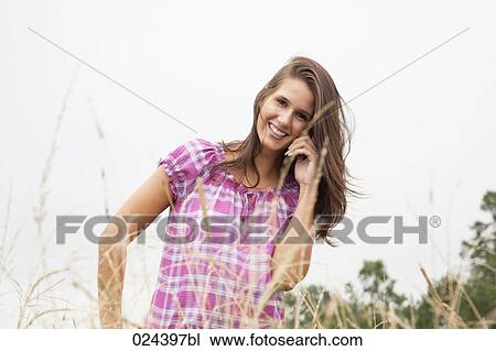 Stock Image - portrait of young woman in field talking on mobile phone. Fotosearch