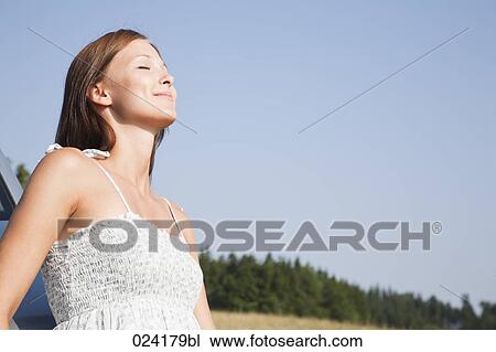 Stock Image - portrait of young woman in summer leaning against car. Fotosearch
