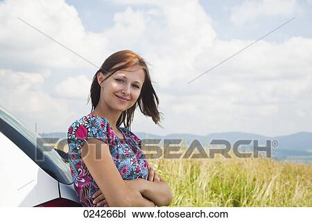 Stock Image - portrait of young woman leaning against car. Fotosearch