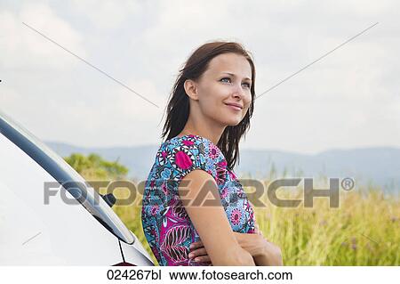 Stock Image - portrait of young woman leaning against car. Fotosearch