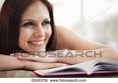 Stock Image - portrait of young woman lying on sofa with book. Fotosearch
