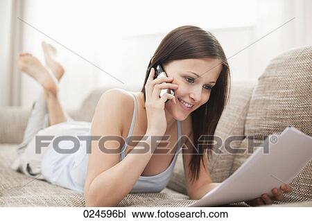 Stock Image - portrait of young woman on sofa talking on mobile phone. Fotosearch