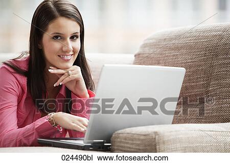 Stock Image - portrait of young woman on sofa working with laptop computer. Fotosearch