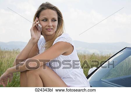 portrait of young woman siiting on bonnet of car talking on mobile phone View Large Photo Image Stock Image - portrait of young woman siiting on bonnet of car talking on mobile phone. Fotosearch