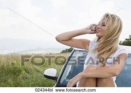portrait of young woman siiting on bonnet of car talking on mobile phone View Large Photo Image Stock Image - portrait of young woman siiting on bonnet of car talking on mobile phone. Fotosearch
