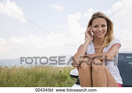 portrait of young woman siiting on bonnet of car talking on mobile phone View Large Photo Image Stock Image - portrait of young woman siiting on bonnet of car talking on mobile phone. Fotosearch