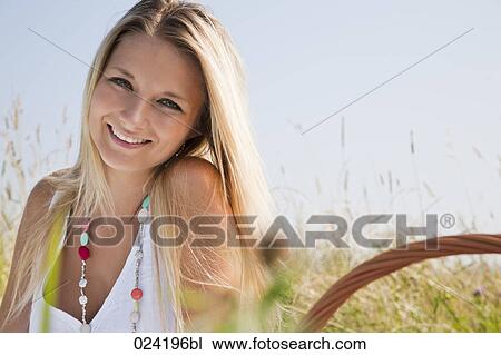 Stock Image - portrait of young woman sitting in meadow having picnic. Fotosearch
