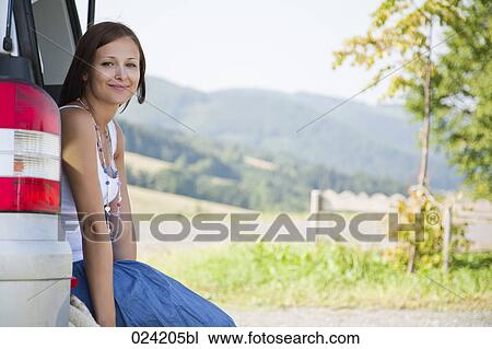 Stock Image - portrait of young woman sitting in trunk of car. Fotosearch