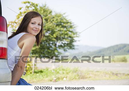 Stock Image - portrait of young woman sitting in trunk of car. Fotosearch
