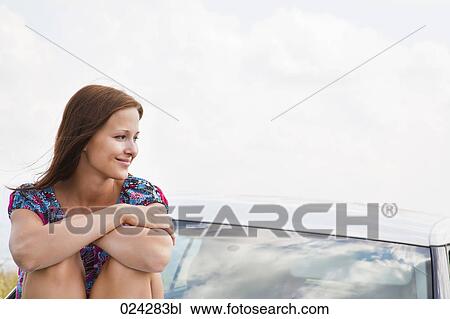 portrait of young woman sitting on bonnet of car View Large Photo Image Stock Image - portrait of young woman sitting on bonnet of car. Fotosearch
