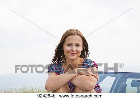 Stock Image - portrait of young woman sitting on bonnet of car. Fotosearch