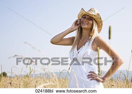 Stock Image - portrait of young woman standing in field talking on mobile phone. Fotosearch
