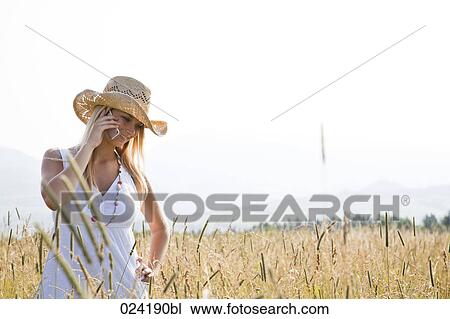 Stock Image - portrait of young woman standing in field talking on mobile phone. Fotosearch