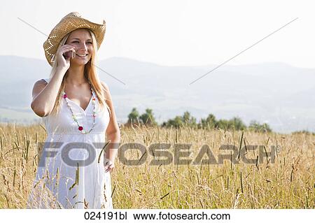 Stock Image - portrait of young woman standing in field talking on mobile phone. Fotosearch