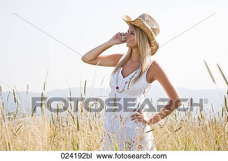 Stock Image - portrait of young woman standing in field talking on mobile phone. Fotosearch