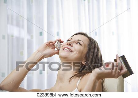 Stock Image - portrait of young woman talking on mobile phone holding credit card. Fotosearch