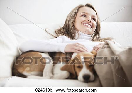 Stock Image - portrait of young woman together on sofa with dog. Fotosearch
