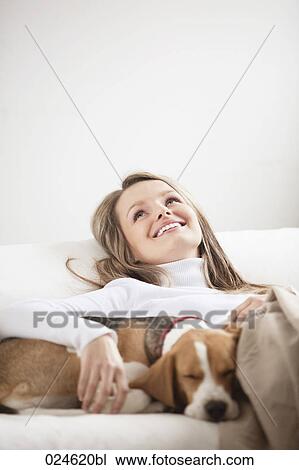 Stock Image - portrait of young woman together on sofa with dog. Fotosearch