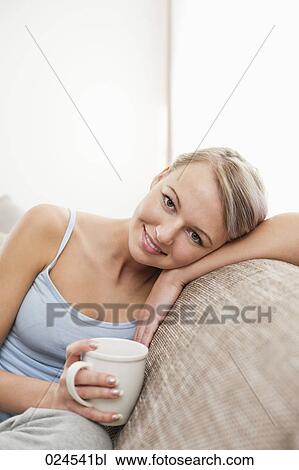 Stock Image - portrait of young woman with coffee cup relaxing on sofa. Fotosearch