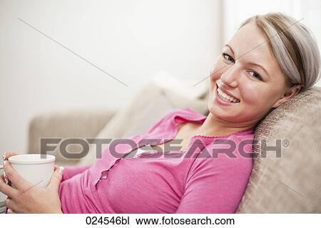 Stock Image - portrait of young woman with coffee cup relaxing on sofa. Fotosearch
