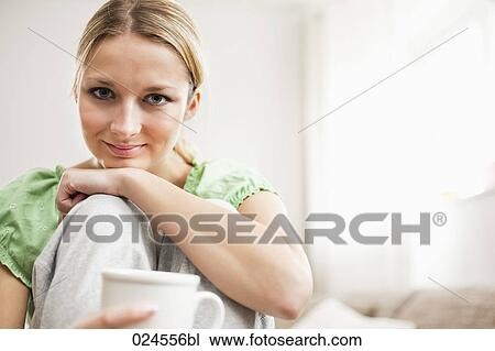Stock Image - portrait of young woman with coffee cup relaxing on sofa. Fotosearch