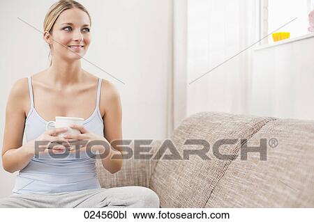 Stock Image - portrait of young woman with coffee cup relaxing on sofa. Fotosearch