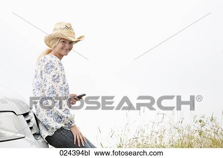 Stock Image - portrait of young woman with mobile phone leaning against car. Fotosearch