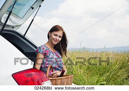 Stock Image - portrait of young young woman with picnic baset at car. Fotosearch
