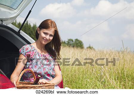 Stock Image - portrait of young young woman with picnic baset at car. Fotosearch