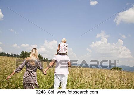 Stock Image - rear view of young family walking through meadow. Fotosearch
