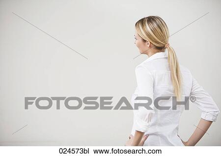 Stock Image - rear view of young woman looking at empty wall. Fotosearch