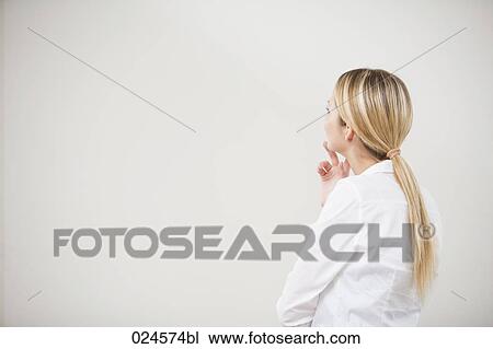 Stock Image - rear view of young woman looking at empty wall. Fotosearch